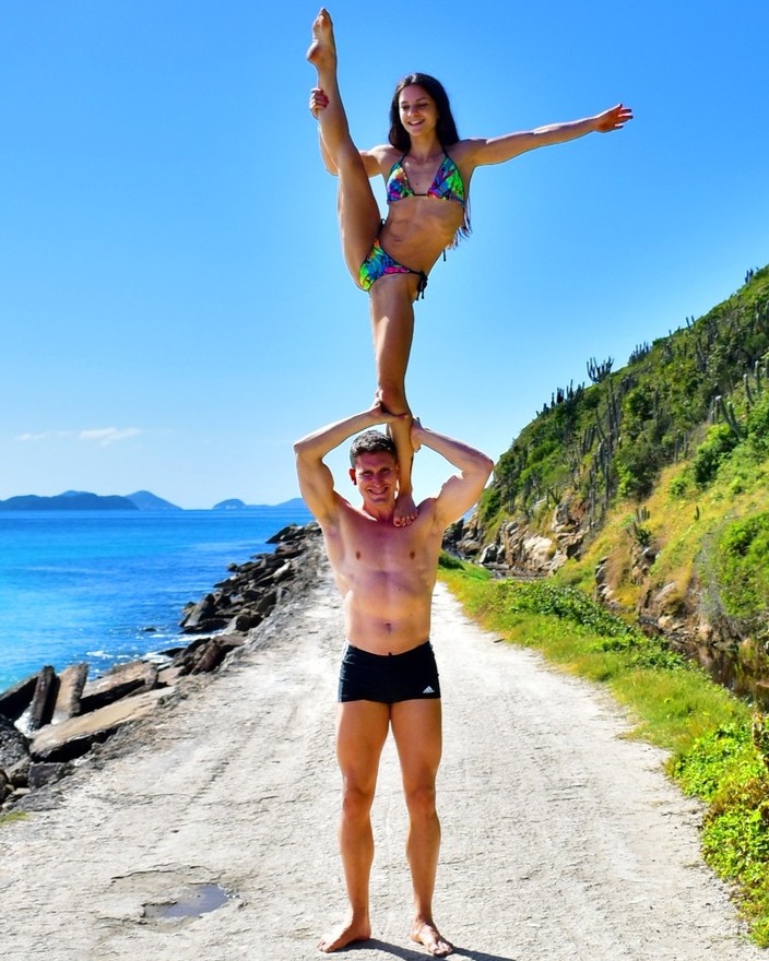 Couple doing an acrobatic balance pose on a coastal road, embracing life abroad