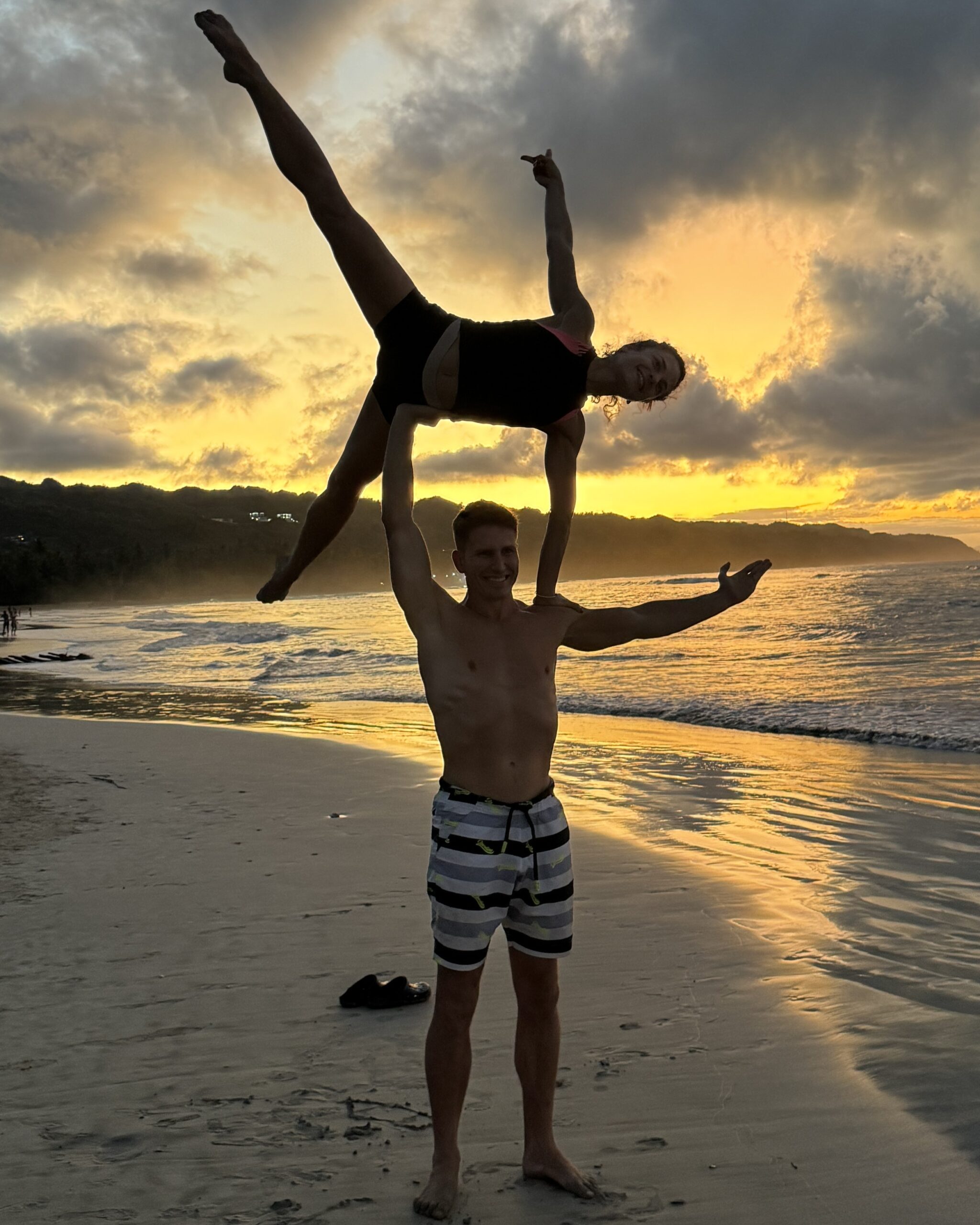 Couple doing an acrobatic pose on the beach at sunset